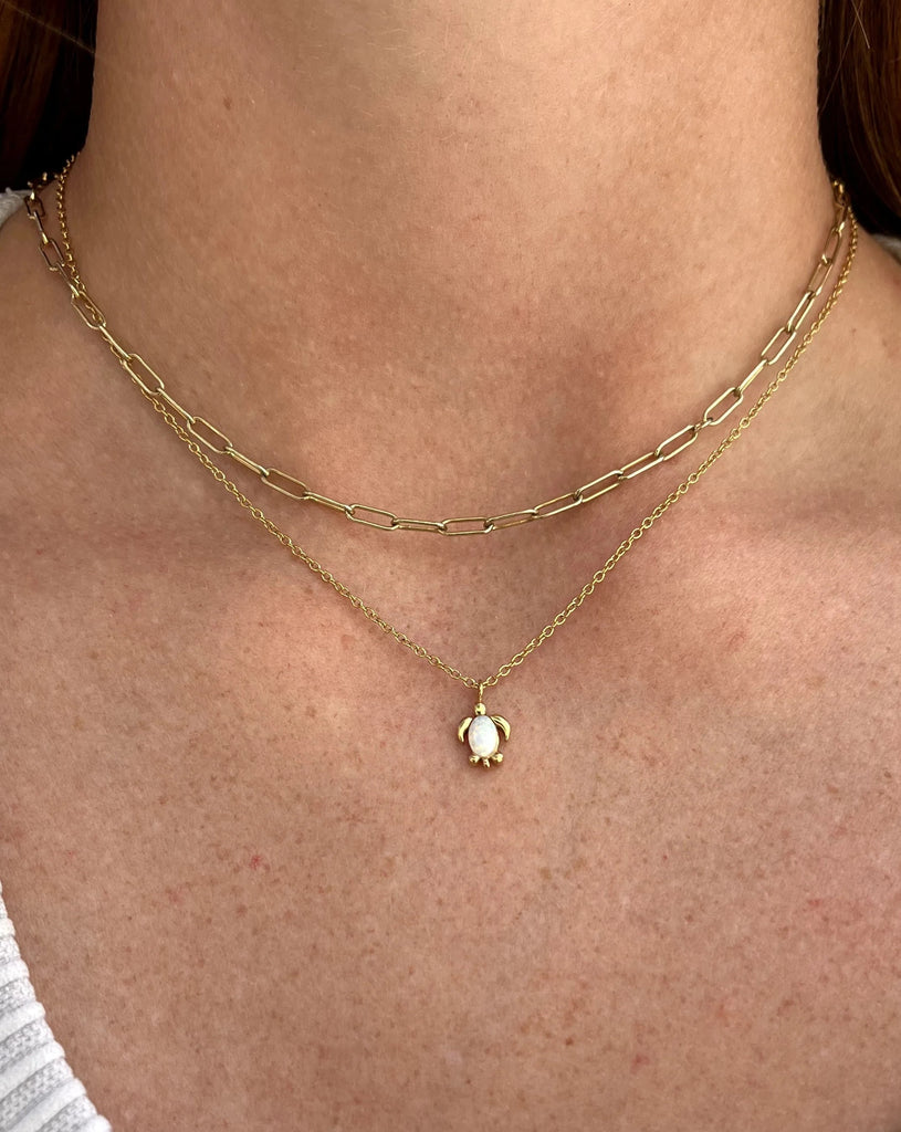 Gold necklace and turtle with opal charm on turtle shell.