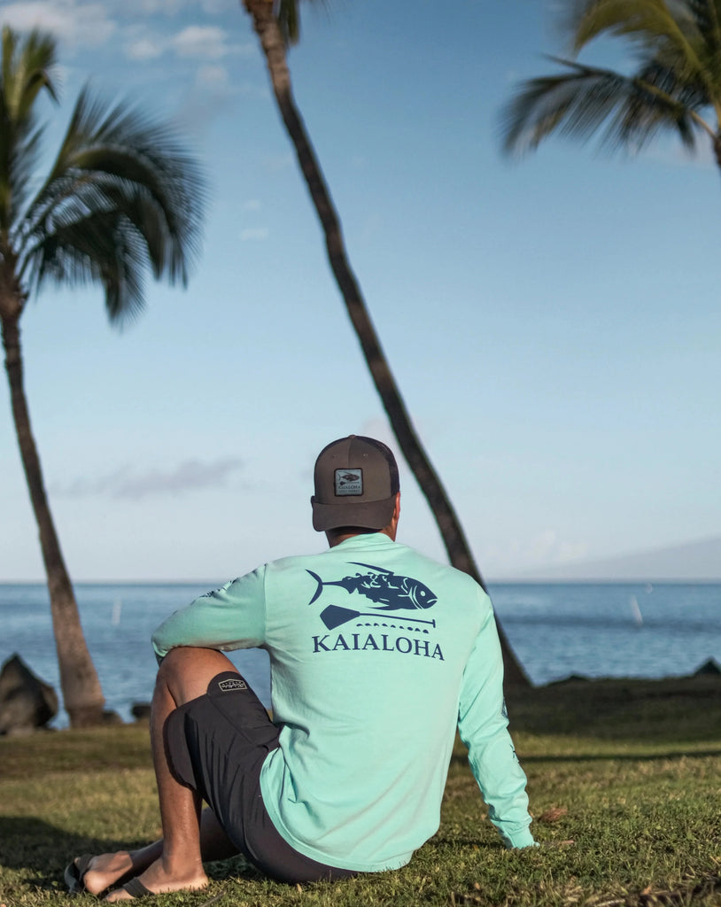The base of this hat is in the color gray. The back snapback is a navy blue. The front has a patch of our Klassic fish design with KaiAloha Maui Hawaii written below the paddle. On the back near the strap adjustment, there is a blue label with the Hawaiian islands in turquoise.